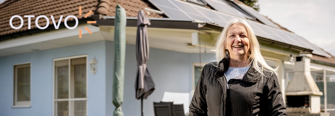 Lächelnde Person vor einem Haus mit Solaranlage